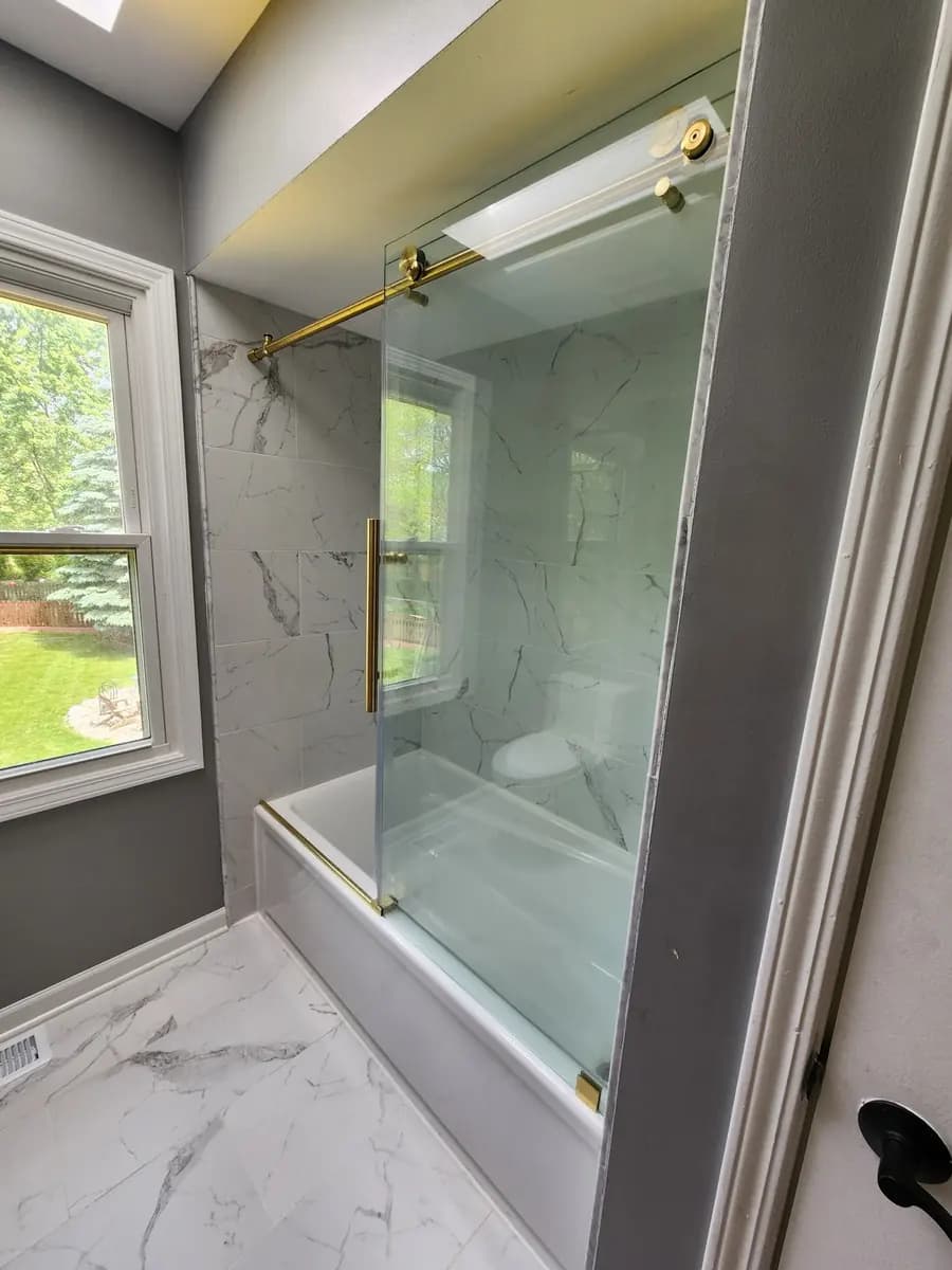 Completed glass tub enclosure with brass rail and finished tile surfaces.